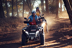 A pair of ATVs being ridden down a trail through the woods