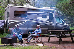A man and woman sitting next to a camp fire next to an RV